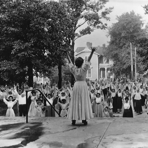 A woman leading out a group of people in breathing exercises while outdoors.