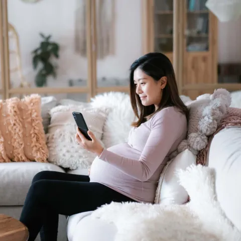 Pregnant woman sitting on couch with phone smiling