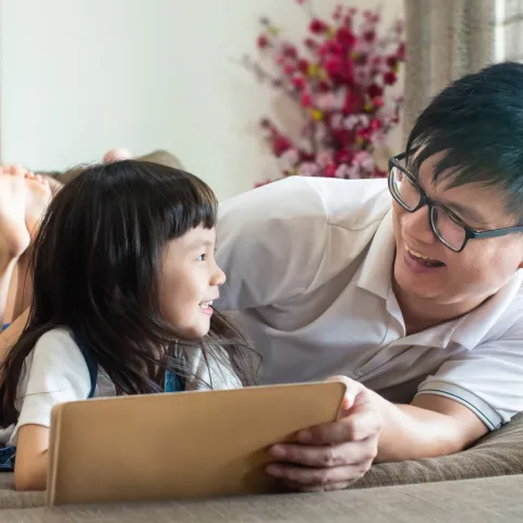 A father and his daughter lying on the floor reading together.
