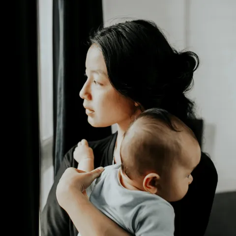 A woman holding her baby looking out the window.