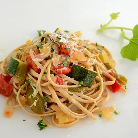 Mound of whole wheat pasta and veggies with leave garnish