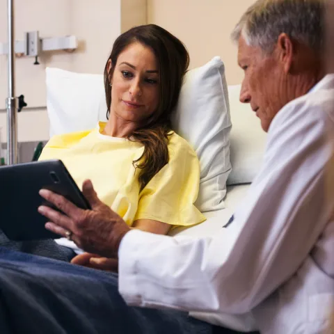 A male doctor goes over a female patient's results on a tablet in her hospital room.