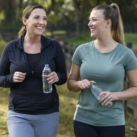 Two women holding water bottles walking together outside 