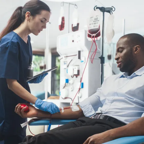A man sitting in a chair donating blood with the help of a nurse.