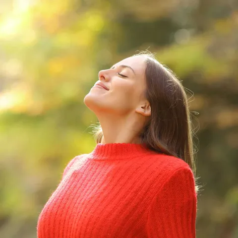 Woman smiling with her eyes closed outdoors.