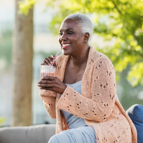 A Black Woman Enjoys a Smoothie on a Bench Outside