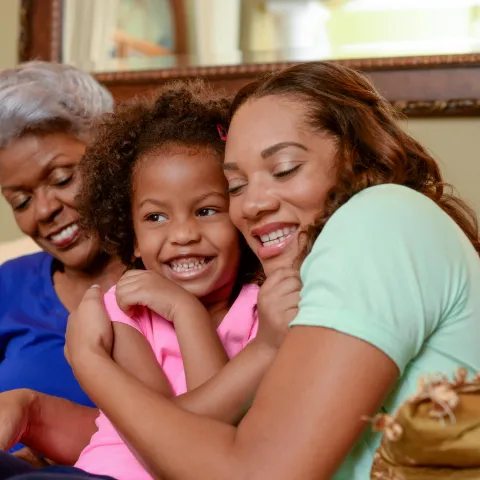 A mother, daughter, and grandmother hug each other on the couch.