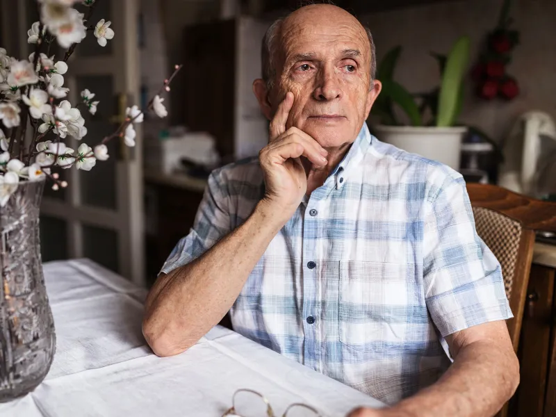 A Man Looks Seriously Out a Window of His Home