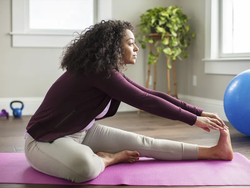 A young African American woman stretches for exercise in her living room.