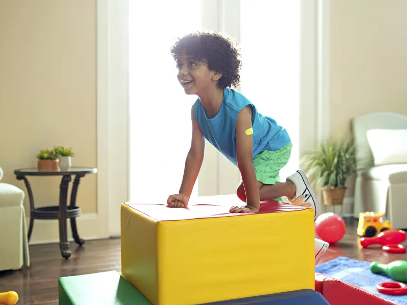 A young African American boy plays on cushioned toy blocks at home.