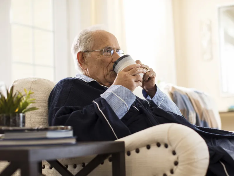 An elderly Caucasian man sips coffee on a couch.