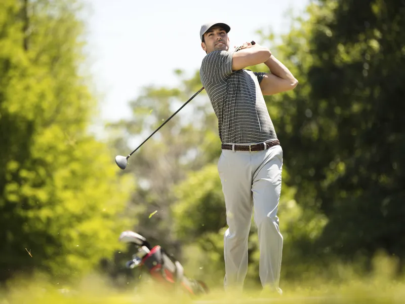 A young Caucasian man golfing on a golf course.