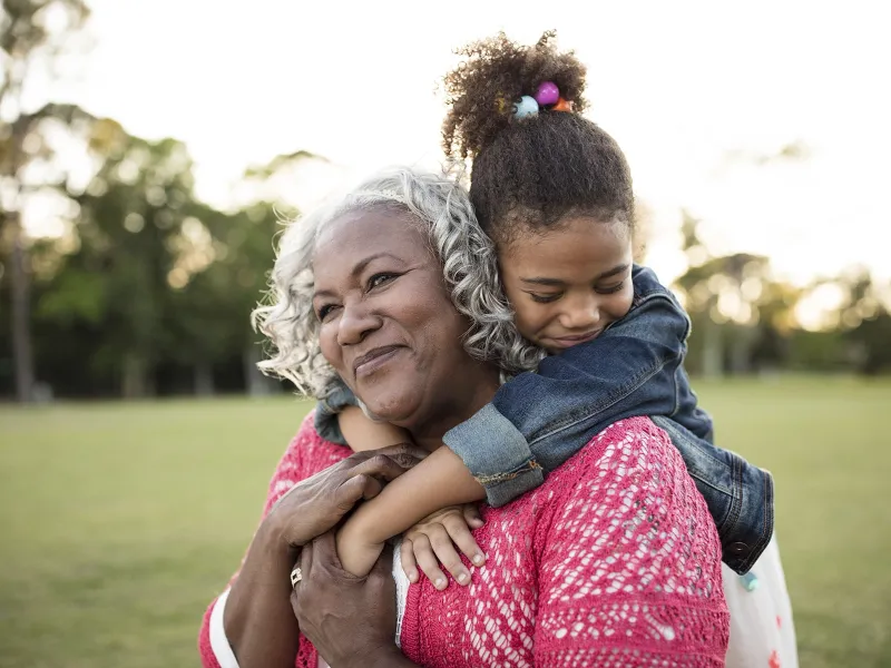 An African American granddaughter embraces her grandmother around the neck.