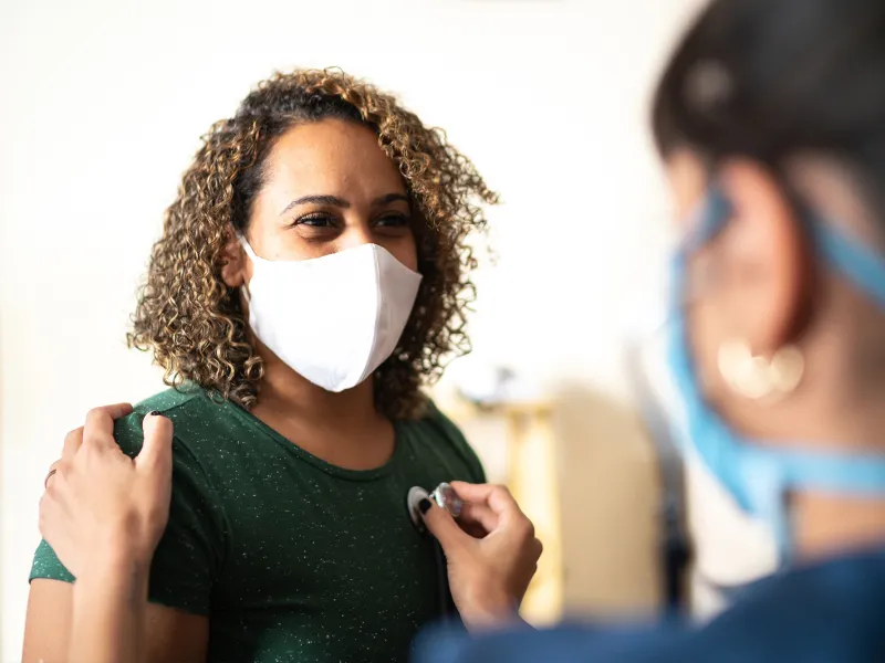 A Woman Wearing a Face Mask has her Vitals Taken by a Care Provider