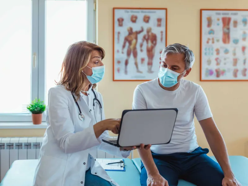 A female doctor pointing at her laptop while showing it to her patient.