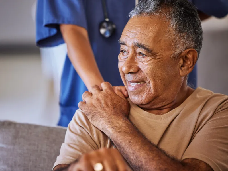 A Senior Man Smiles as a Nurse Puts Her Hand on His Shoulder for Comfort.