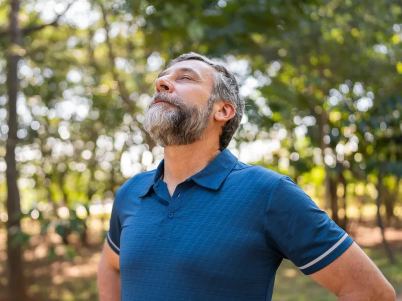 A Man Takes a Deep Breath Outdoors in the Woods