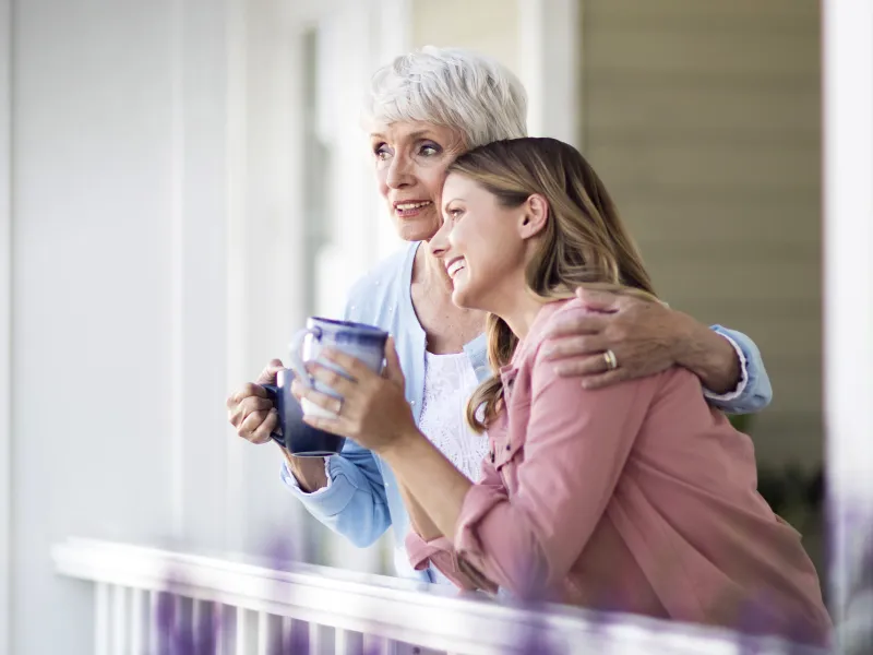 Two women converse on the front porch while drinking coffee.