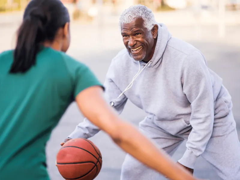 A Senior Man Plays Basketball with an Adult Child