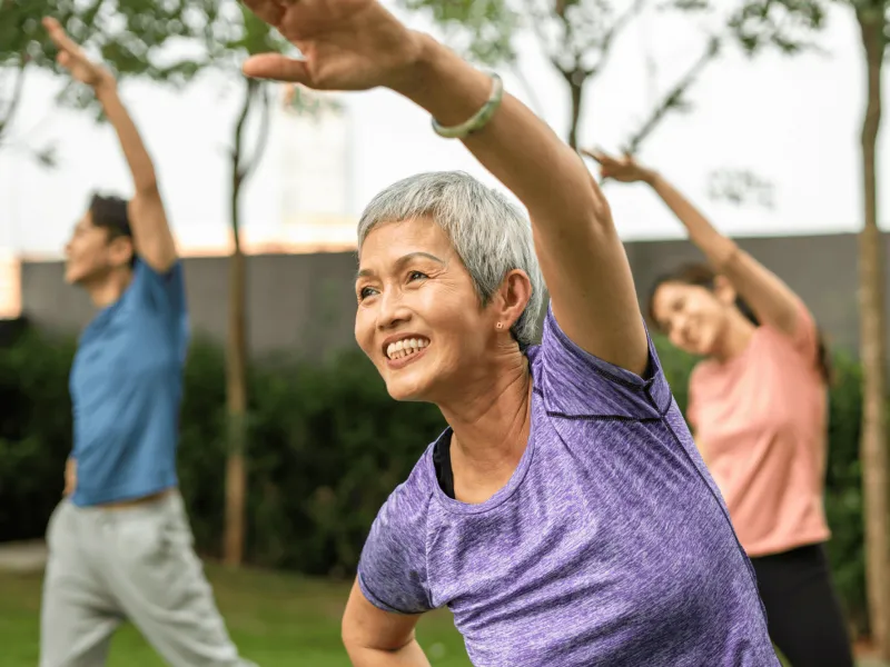 A Senior Woman Does Group Yoga in a Park