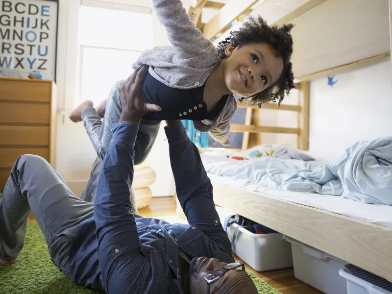 An African American father plays airplane with his daughter.