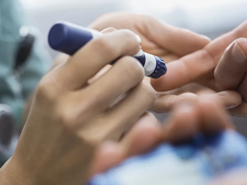 A diabetic patient takes a finger prick reading from an insulin pen.