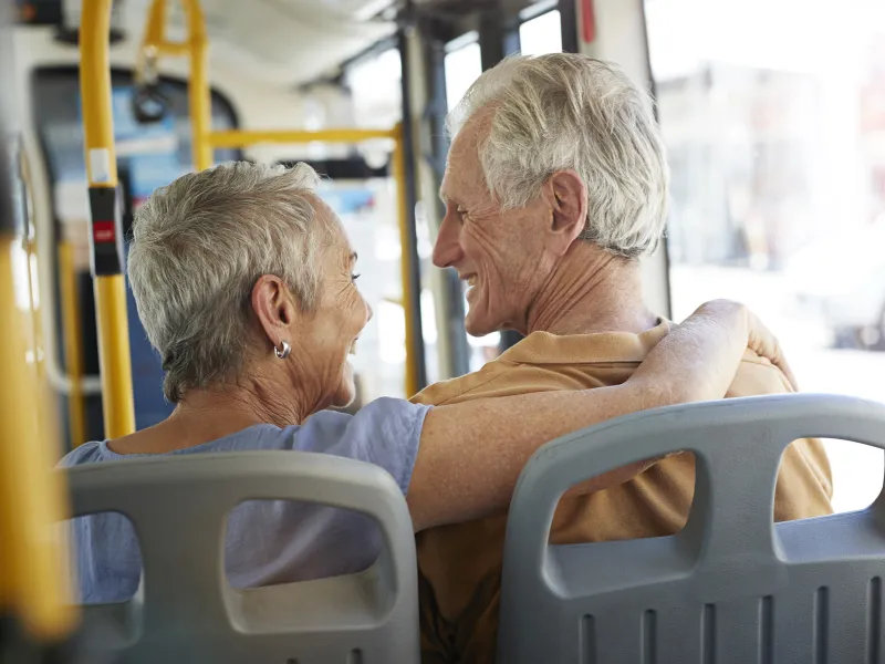 An elderly Caucasian couple rides on the bus on a sunny afternoon.