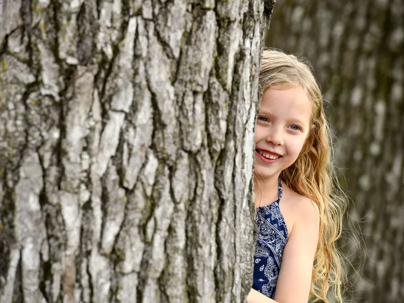 Girl Peeks Out From Behind A Tree