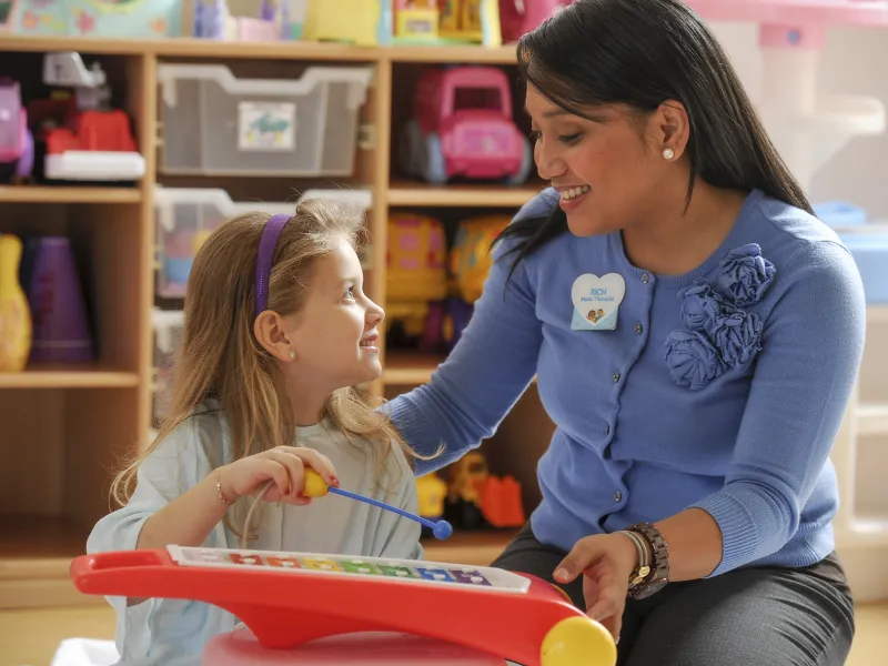 A young Caucasian girl plays the xylophone with her Asian music therapist.