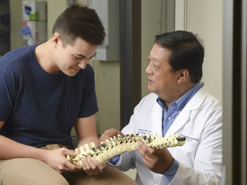 A doctor showing a spine skeleton to a young male patient.
