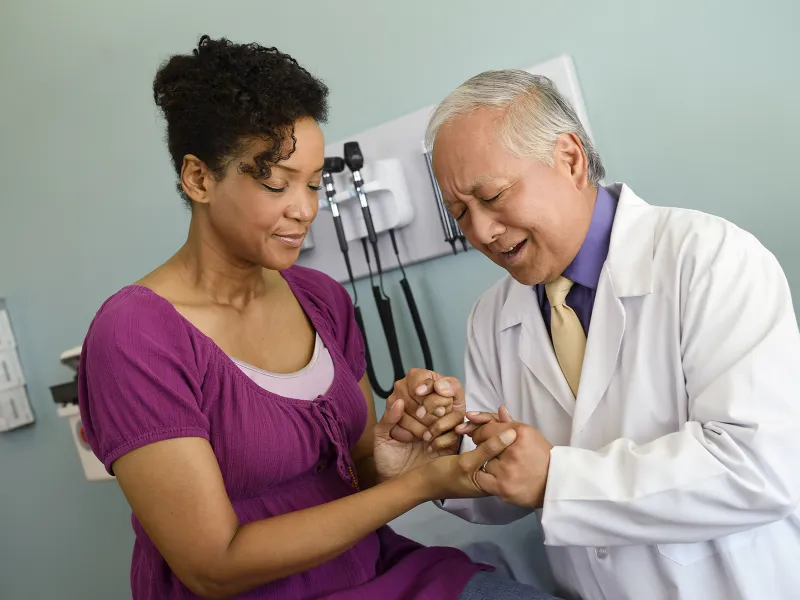 An Asian doctor prays with an African-American woman at the hospital.