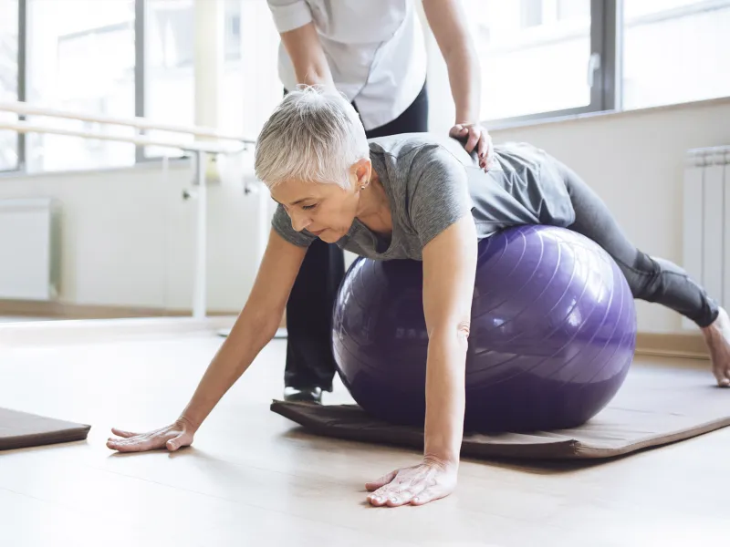 A Caucasian woman balances herself on an exercise ball.