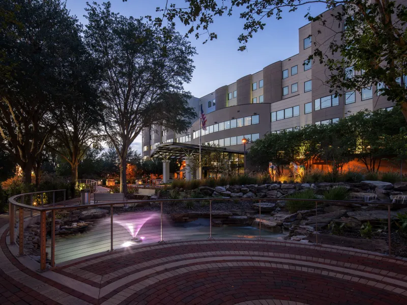 A photo of AdventHealth Ocala taken at dusk. A brick walking path with a railing is in the foreground and the hospital is in the background. 