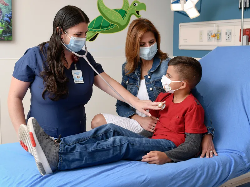 Nurse checking child's heartbeat at AdventHealth Fish Memorial Pediatric ER while his mother stands nearby.