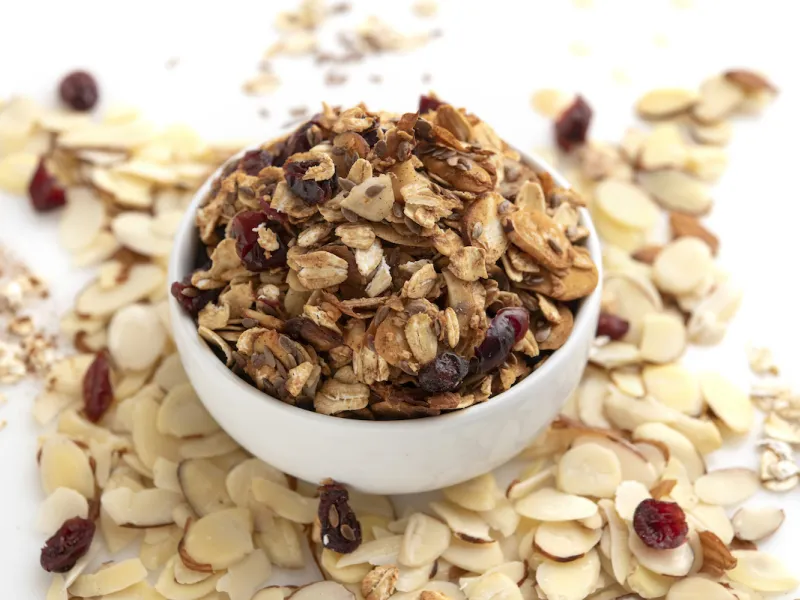 White bowl of granola surrounded by sliced almonds