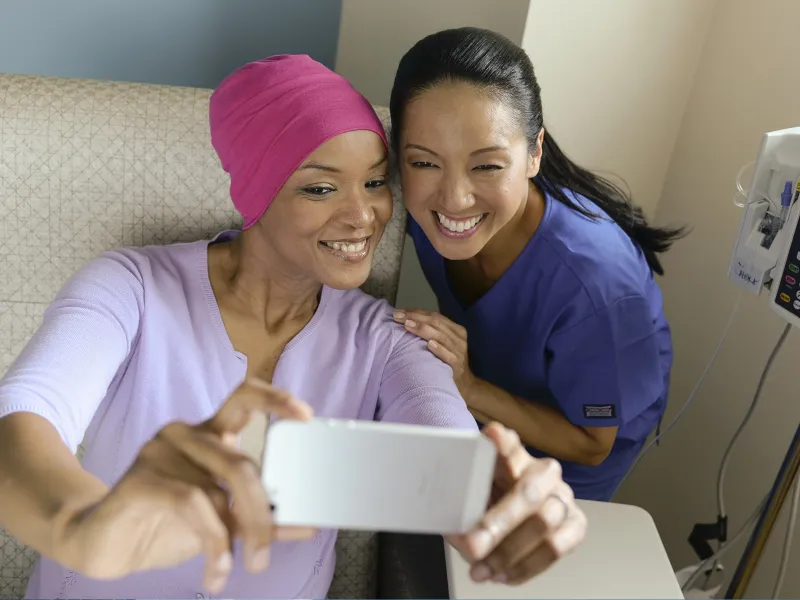 A female African American cancer patient takes a selfie with a female Asian nurse.