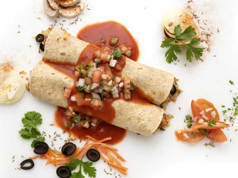 Two enchiladas with sauce and parsley, carrot, and olive garnishes