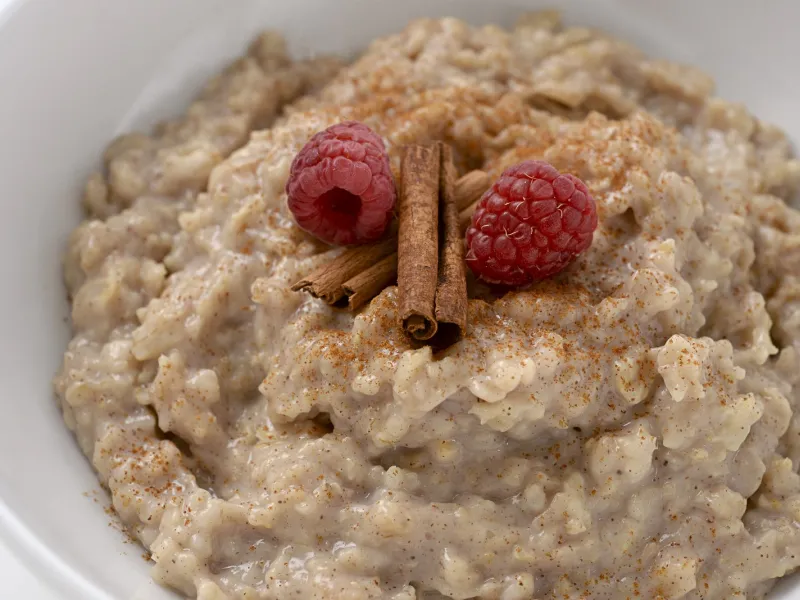 a bowl filled with a sweet cinnamon oatmeal mixture, topped with two raspberries and a cinnamon stick