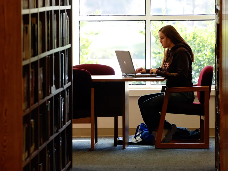 A girl sitting at a table in the library on her laptop.