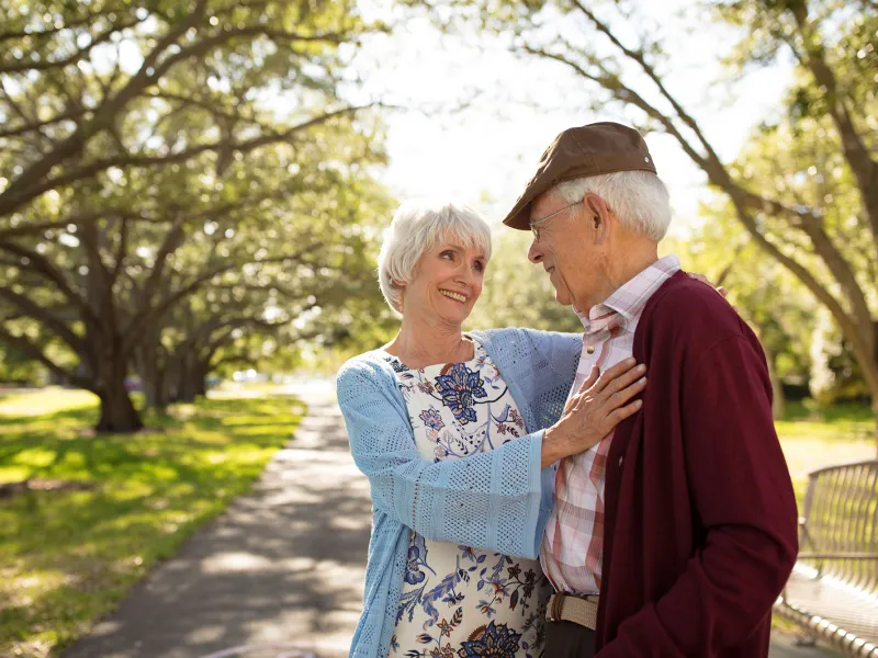 An elderly couple hugging each other at the park. 