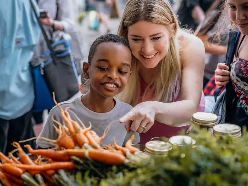 A young lady and a little boy pointing at carrots.  