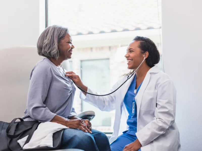 Doctor listening to an older woman patient's heart.
