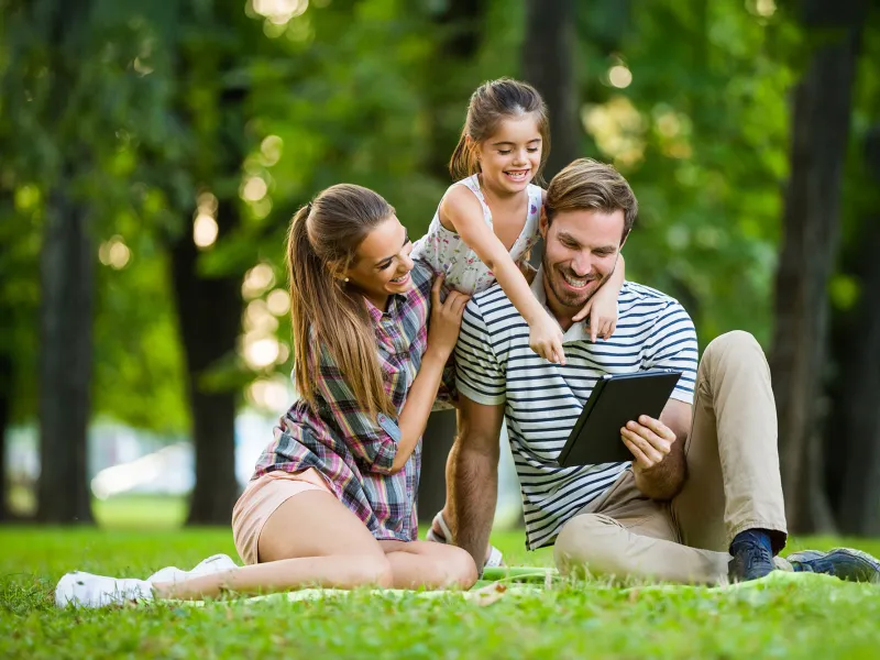 Family Sitting in a Park Looking at a Tablet