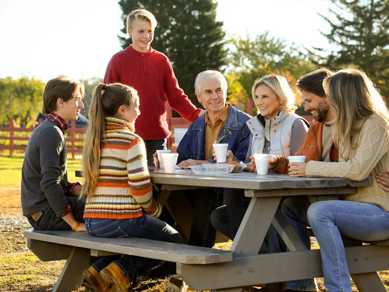 Family sitting outside at a picnic table having a meal.