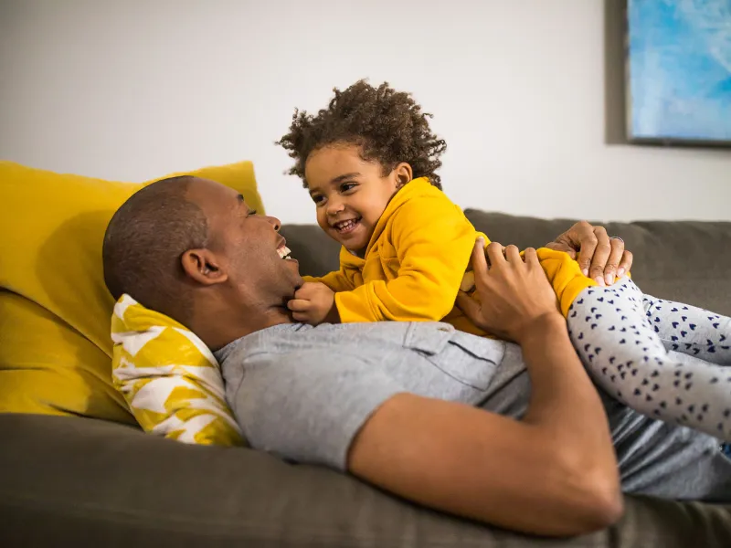 A dad is embracing his baby while they are laying down on the couch.