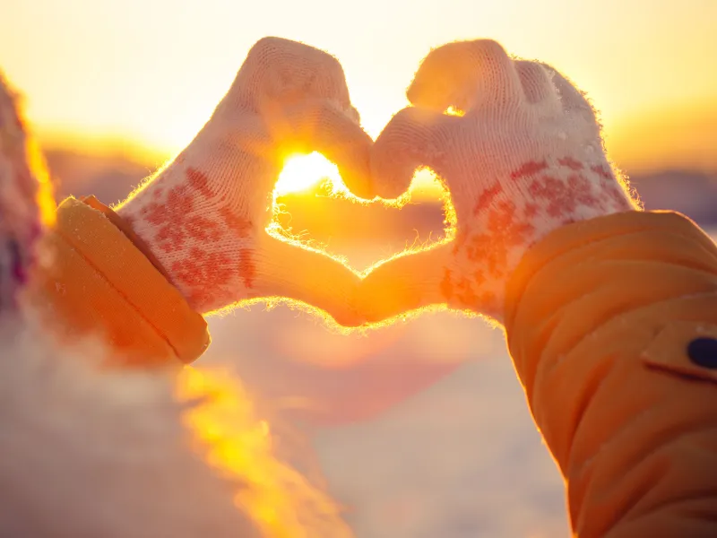 Woman in winter clothing making a heart with her hands.