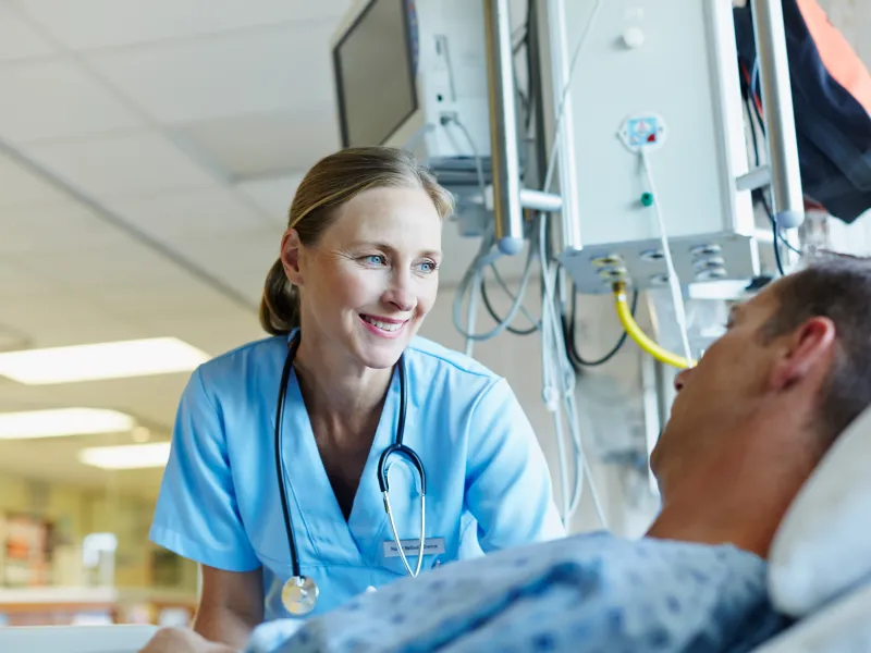 A smiling female physician reassures her male patient in a hospital room.