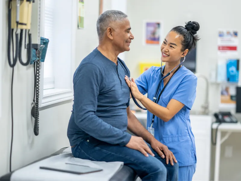 An older Hispanic man gets examined by a nurse.