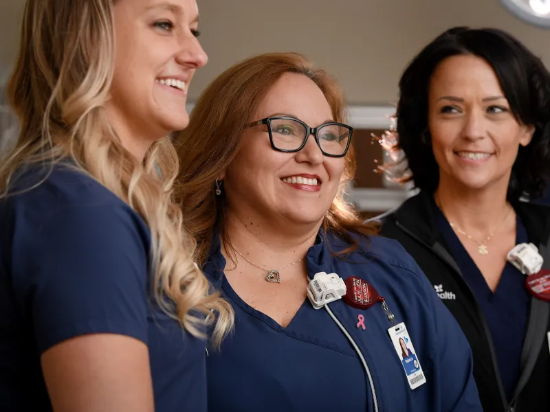 Three nurses stand together, smiling at something off the right side of the image.
