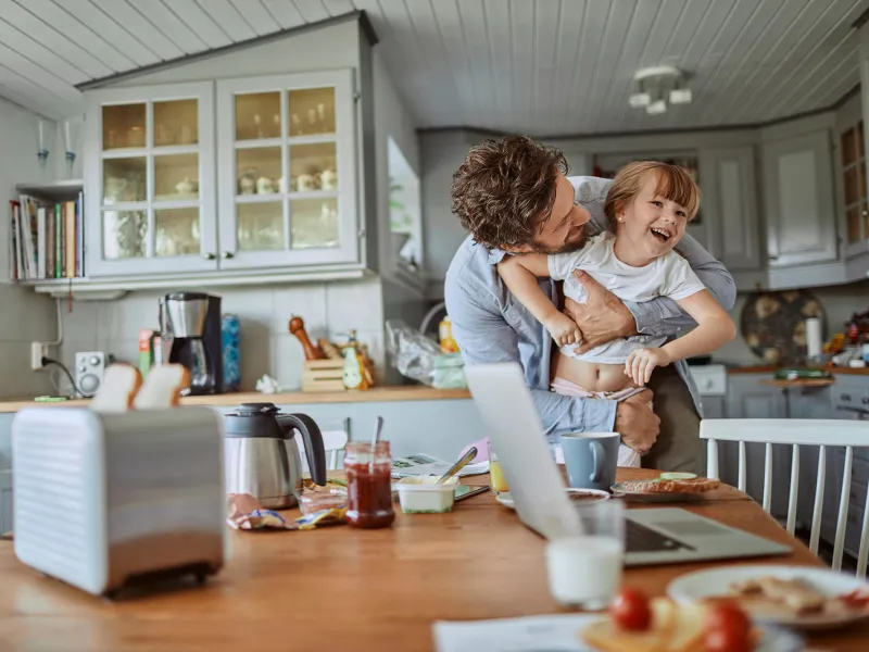 Father holding daughter while they both laugh next to dining table